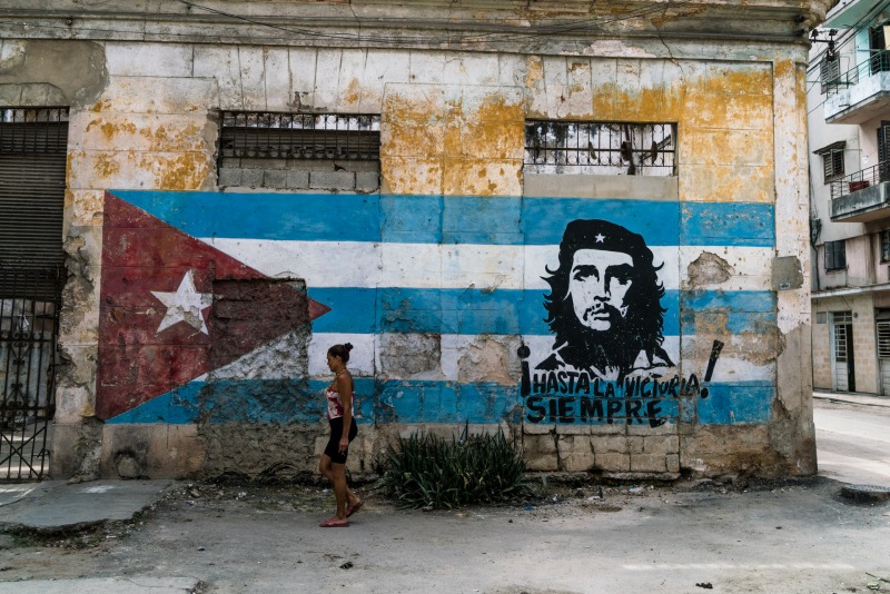 A cuban woman walks past street art depicting the Cuban flag and a portrait of Che Guevara in Havana Cuba.