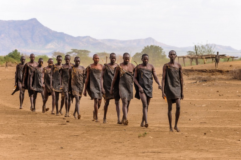 Men from the Kara tribe, who are bull jumpers,  walk single file into Dus Village just prior to taking part in the bull jump ceremony.  They are only allowed to wear a single goat skin and no shoes for a year leading up to this day.